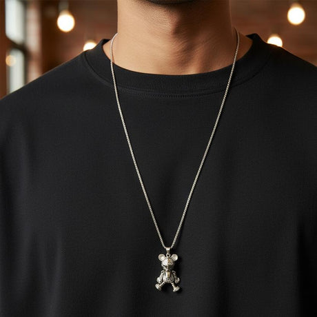 Teddy bear pendant necklace worn over a black tee under warm lighting