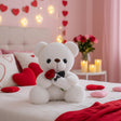 White plush bear holding a red rose tied with a polka dot ribbon on a decorated bed