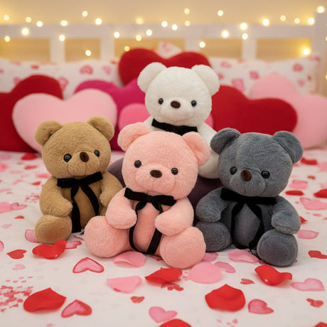 Four small teddy bears in caramel, pink, white and grey, each with a black ribbon bow