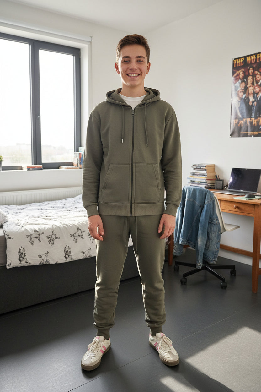 Teen boy wearing a khaki green zip up hoodie and matching joggers standing in a bedroom