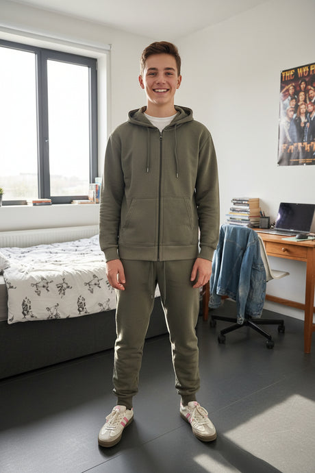 Teen boy wearing a khaki green zip up hoodie and matching joggers standing in a bedroom