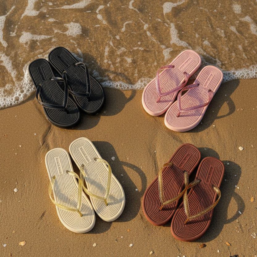 Four pairs of sandals in black, pink, beige, and brown with gold straps on sand