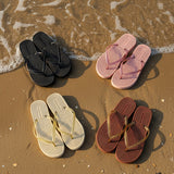 Four pairs of sandals in black, pink, beige, and brown with gold straps on sand