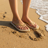 Beige sandals with gold straps on a sandy surface
