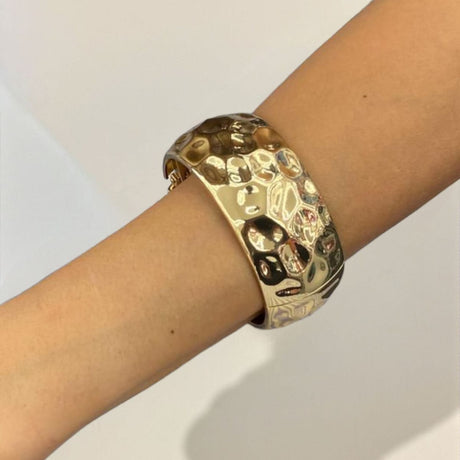Textured gold cuff bracelet on a person's wrist against a plain background