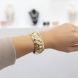 Textured gold cuff bracelet on a wrist with a store interior in the background