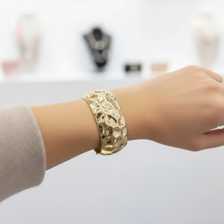 Textured gold cuff bracelet on a wrist with a store interior in the background