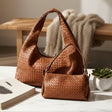 Brown woven handbag on a table with a book and plant in the background