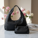 Black woven handbag and matching pouch on a marble surface with flowers in the background