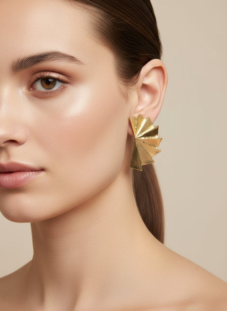 Gold geometric earring worn by a model on a beige background