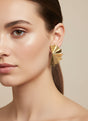 Gold geometric earring worn by a model on a beige background