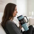 Dusty blue matte tumbler with a black lid, loop handle and cream straw