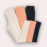 Three pairs of leggings in beige, peach, and black on a light grey background