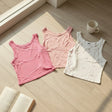 Three tank tops in pink and white on a wooden floor with a cup and book.