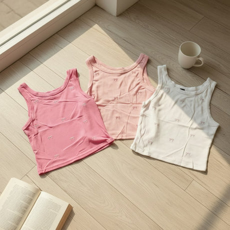 Three tank tops in pink and white on a wooden floor with a cup and book.