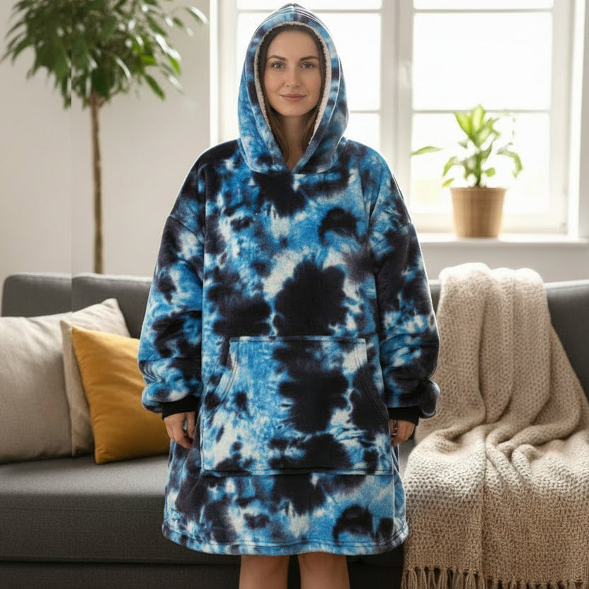 Standing before a grey sofa in a cobalt and white marbled blanket, hood raised, plant behind