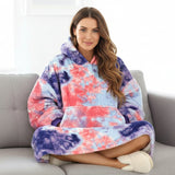 Cross legged on a grey sofa in fluffy slippers, wearing a coral and indigo marbled blanket