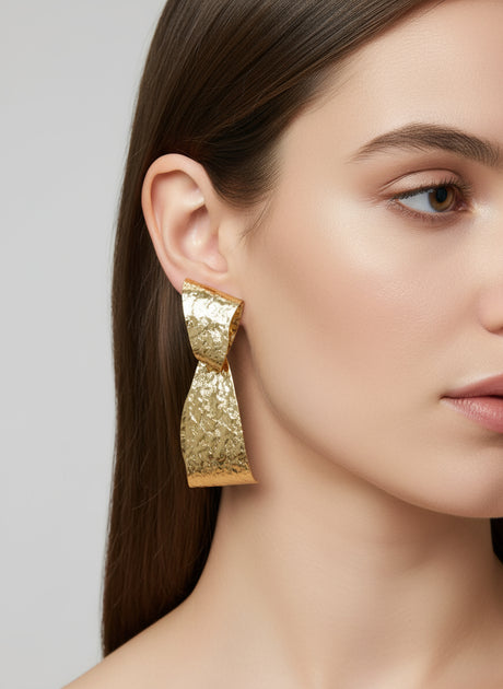 Gold timeless charm earring worn by a model on a plain background