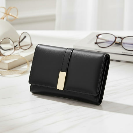 Black wallet with gold accent on a light wooden surface with glasses and books in the background