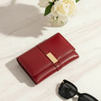Red wallet with gold accent on a light surface next to sunglasses and flowers