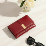 Red wallet with gold accent on a light surface next to sunglasses and flowers