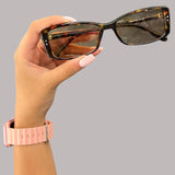 Hand holding a pair of tortoise slim sunglasses with a grey background