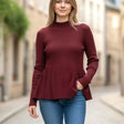 Red mock neck peplum top in fitted rib knit, flared at the waist, worn on a city street
