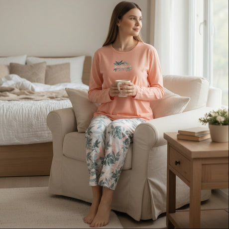 Woman in a peach floral pyjama set sitting on a chair with a mug in a cozy living room