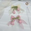 Two organza bows with green stems and satin tulip buds, one ivory and one pink, on a marble surface