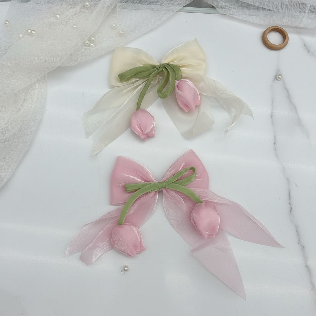 Two organza bows with green stems and satin tulip buds, one ivory and one pink, on a marble surface