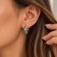 Turquoise enamel hoop earring with gold dots and a textured gold band worn on the ear