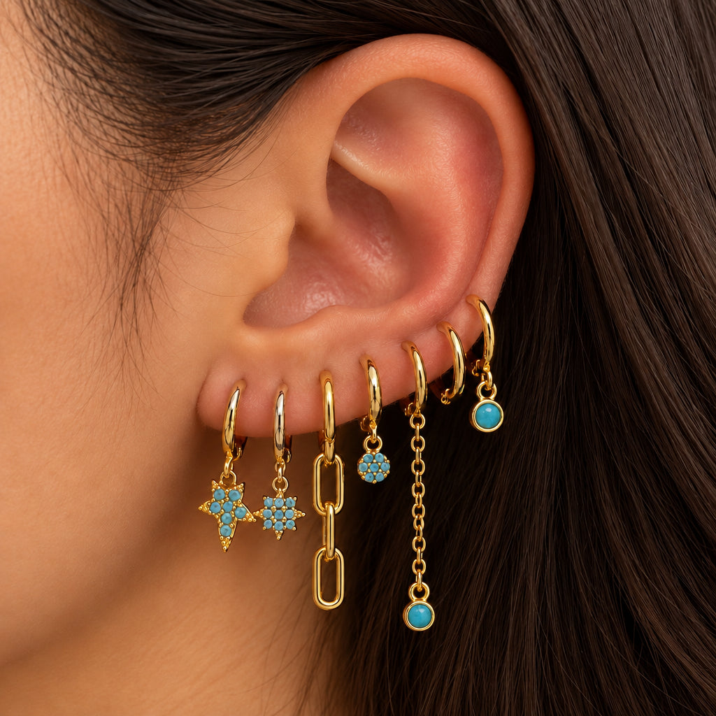 Ear stacked with six gold huggies with turquoise star, flower and round charms and chain drops