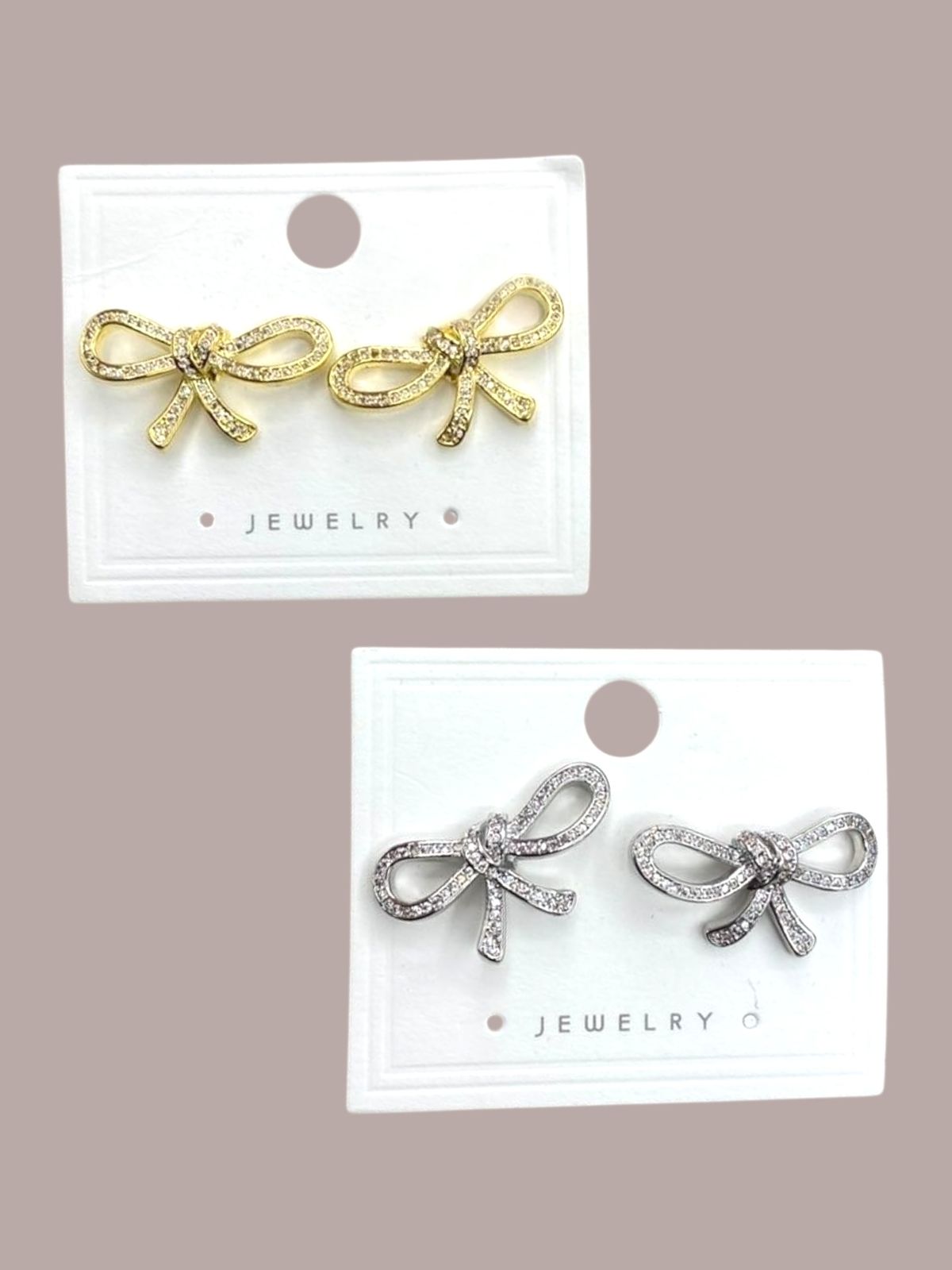 Gold and silver bow-shaped earrings on white cards against a beige background