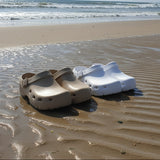 Beige and white clogs on a sandy beach with ocean waves in the background