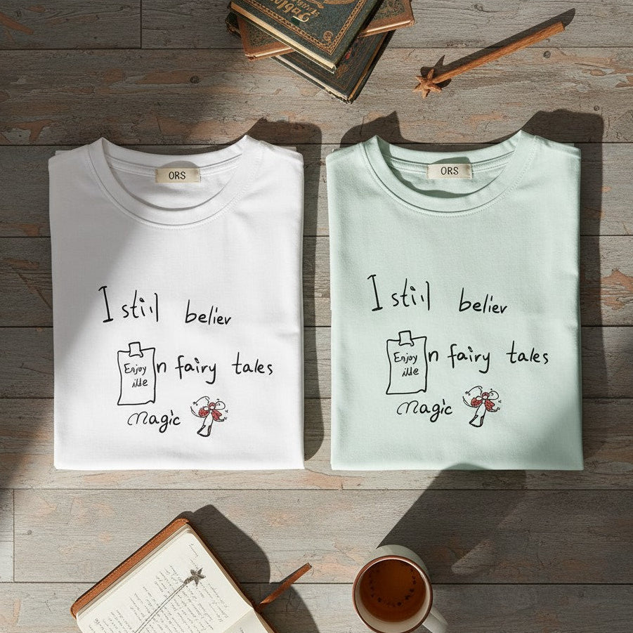 Two sleeveless shirts with text and graphics on a wooden surface with books and a cup.