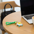 Green strap keychain with a unicorn charm and gold bell resting on a wooden desk