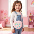 Girl wearing a fluffy pink plush unicorn cross body bag with a mint mane over denim overalls