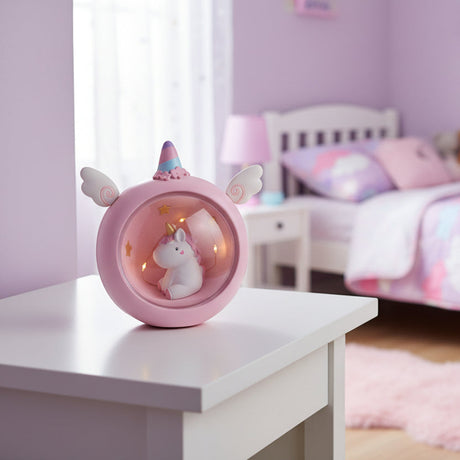 Round pink unicorn night light with wings and a rainbow horn glowing on a white bedside table