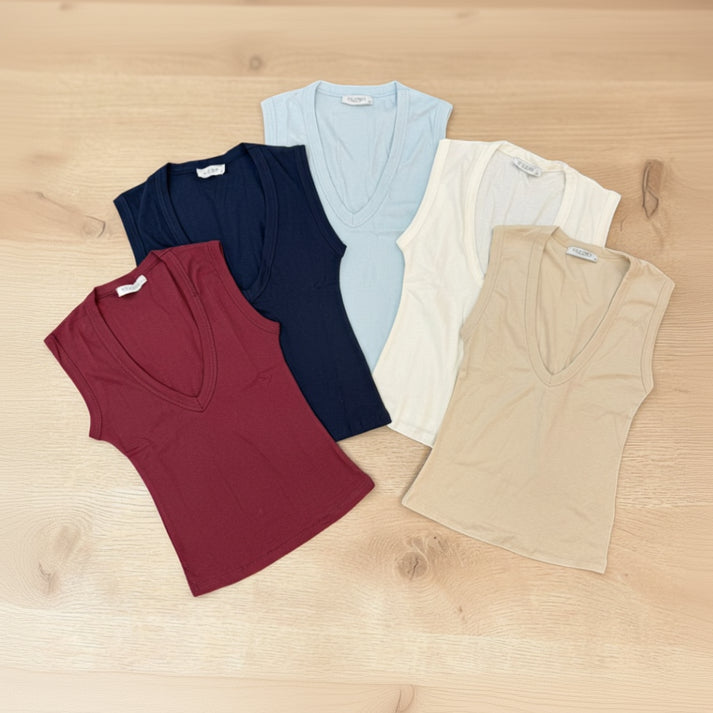 Five V-neck tops in red, navy, light blue, white, and beige on a wooden surface