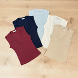 Five V-neck tops in red, navy, light blue, white, and beige on a wooden surface