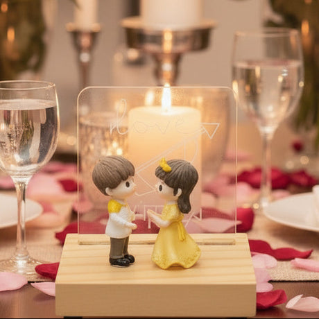 Boy and girl figurines on a wooden stand with a clear panel, candles behind