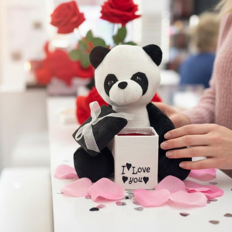Panda plush holding a small black ribboned parcel behind an open white gift box