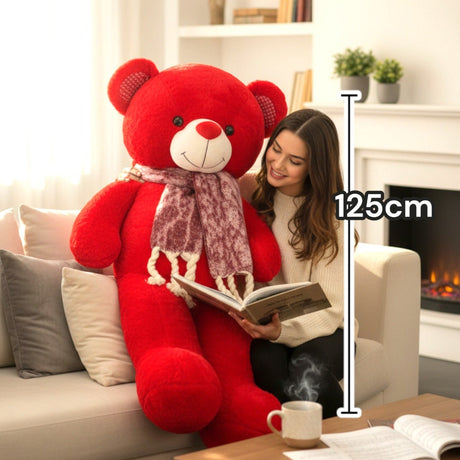 Red teddy bear in a fringed burgundy scarf seated beside a woman reading