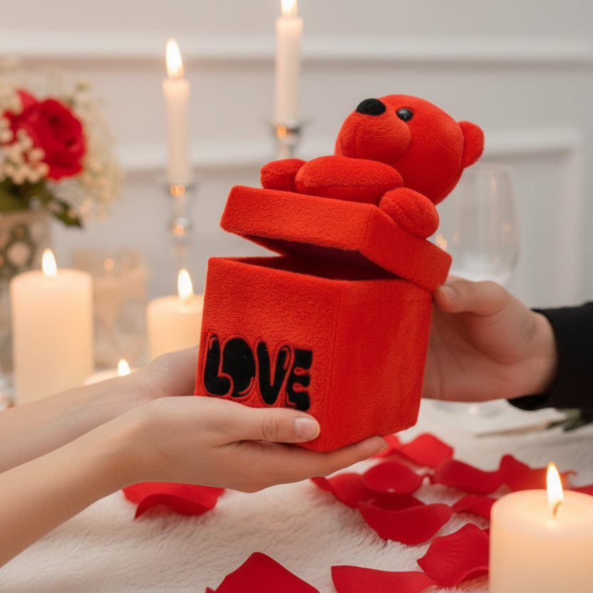 Small red bear emerging from a plush Love gift cube passed between two pairs of hands