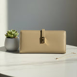 Beige wallet on a marble surface with a potted plant and necklace in the background