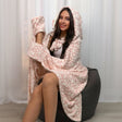 Woman wearing a pink polka dot robe sitting on a bean bag chair against a white curtain background.