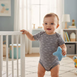Smiling baby at a crib rail in a grey bodysuit with small white wave squiggles, holding a soft blue star