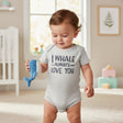 Baby in a grey short sleeve bodysuit with a whale slogan print, holding a soft blue and white plush whale