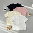 Four t-shirts in black, pink, yellow, and white with heart patterns on a gray surface.
