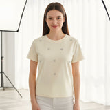 Woman wearing a cream-colored t-shirt with small decorative buttons against a white background